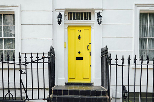 yellow door between about two windows on white house with black fence