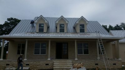 construction workers providing roof replacement services on brick house with light gray metal roof 